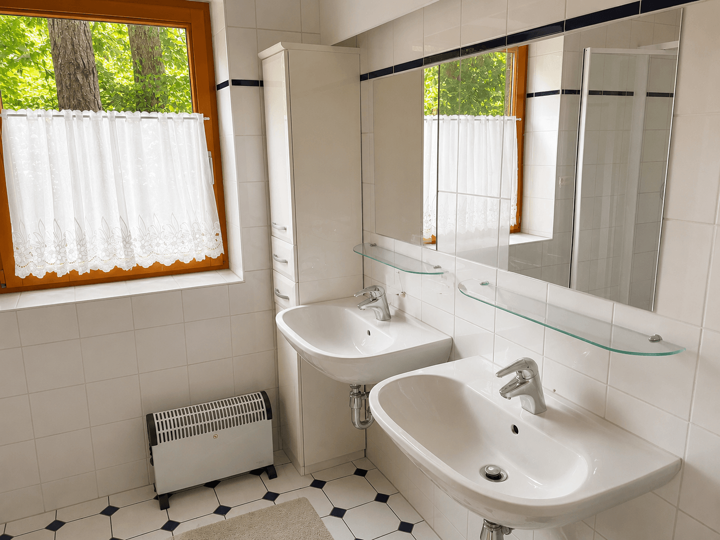 Badezimmer mit Doppelwaschbecken, weißen Fliesen und einem Fenster für natürliches Licht.