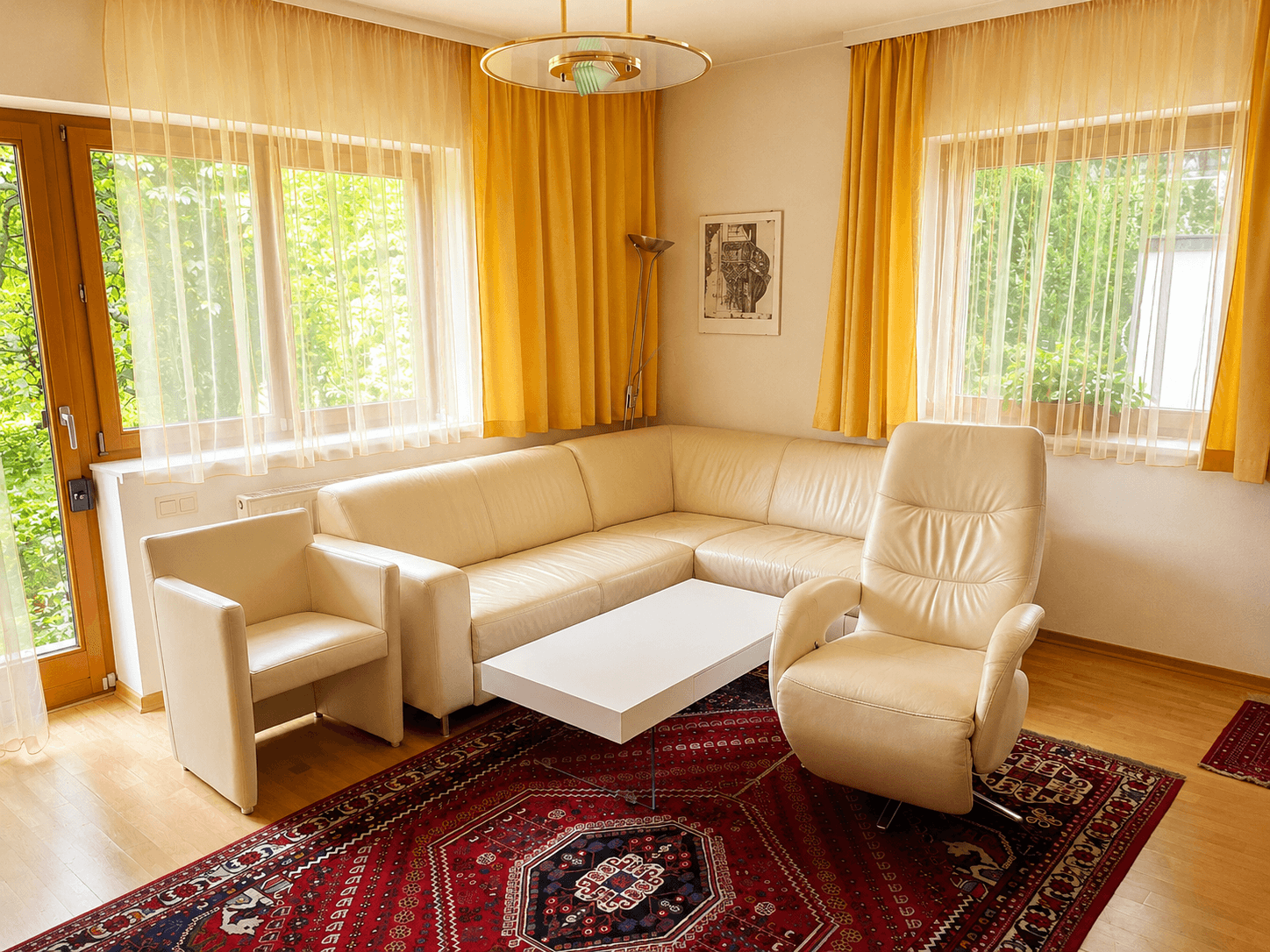 Helles Wohnzimmer mit beigem Ledersofa, Parkettboden und Zugang zu einem Außenbereich.