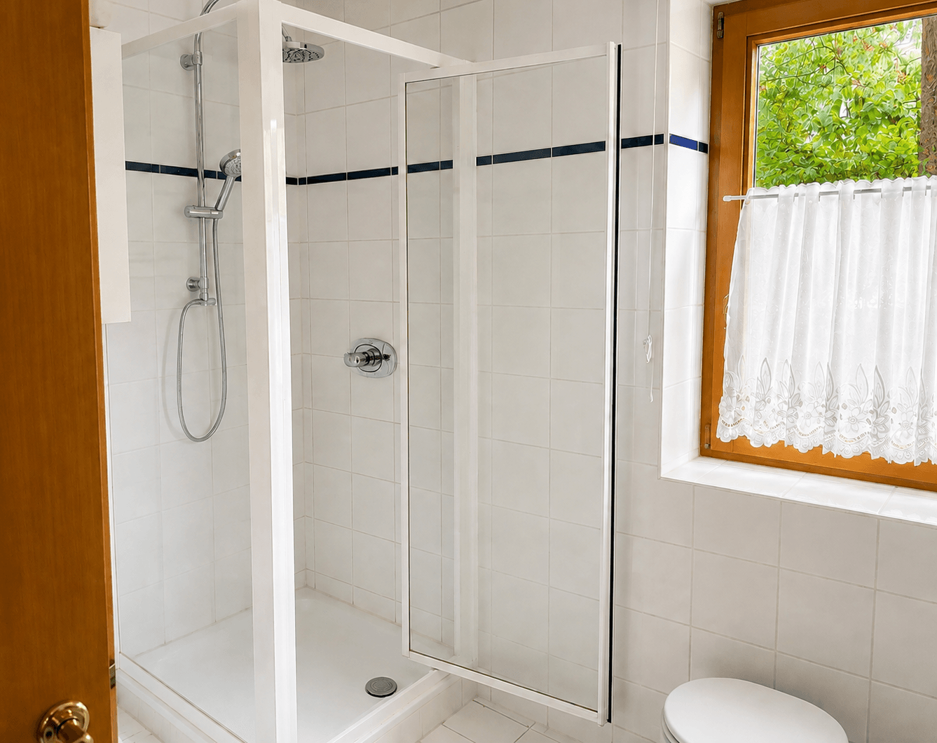 Modernes Badezimmer mit Duschkabine, weißen Fliesen und Fenster, das viel Tageslicht hereinlässt.