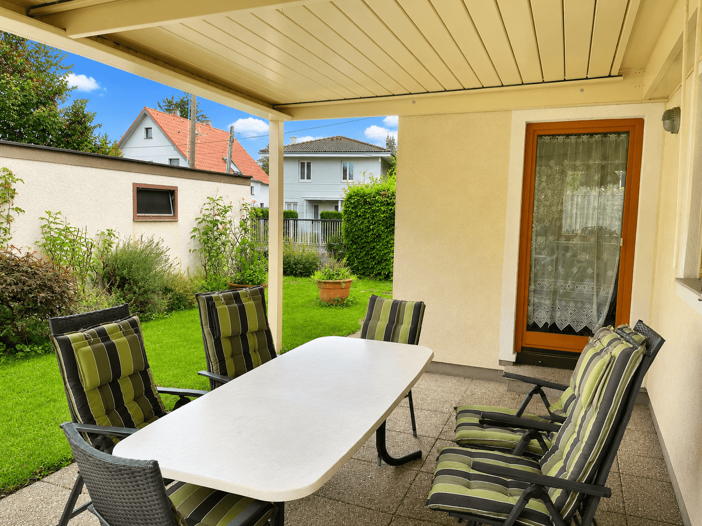 Überdachte Terrasse mit Gartenmöbeln und Blick auf den gepflegten Garten und die Nachbarschaft.