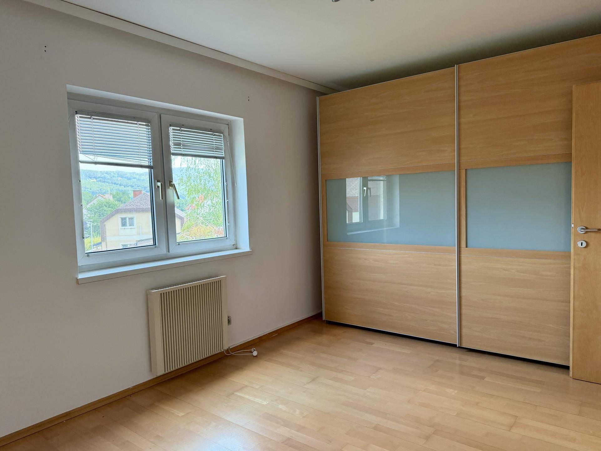 Schlafzimmer mit Einbauschrank, Fenster mit Grünblick und Laminatboden, bietet viel Stauraum.