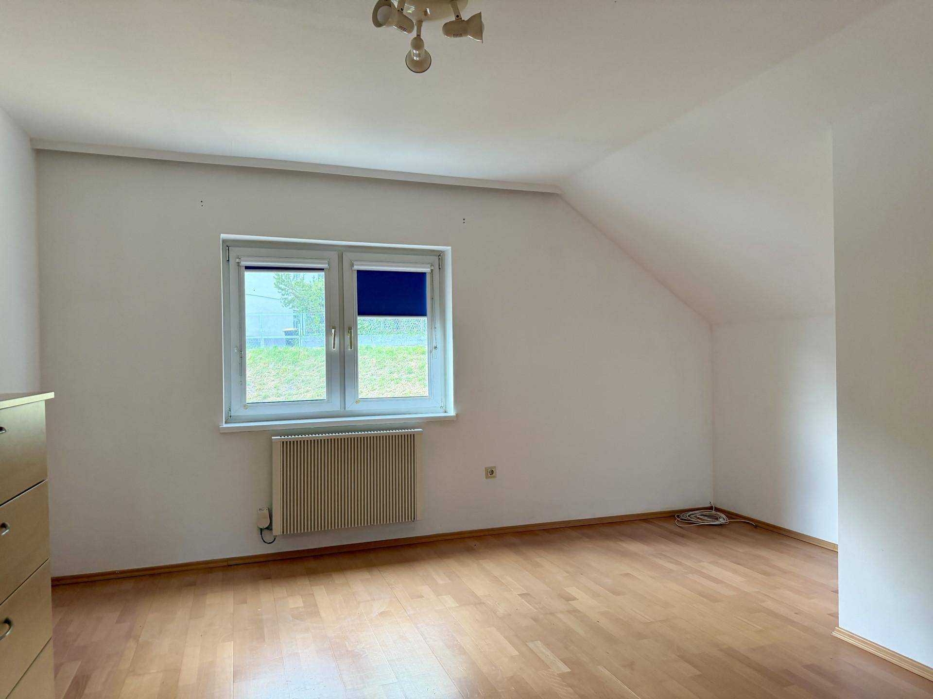 Helles Schlafzimmer mit Dachschräge, Fenster und Heizkörper, bereit zur individuellen Gestaltung.