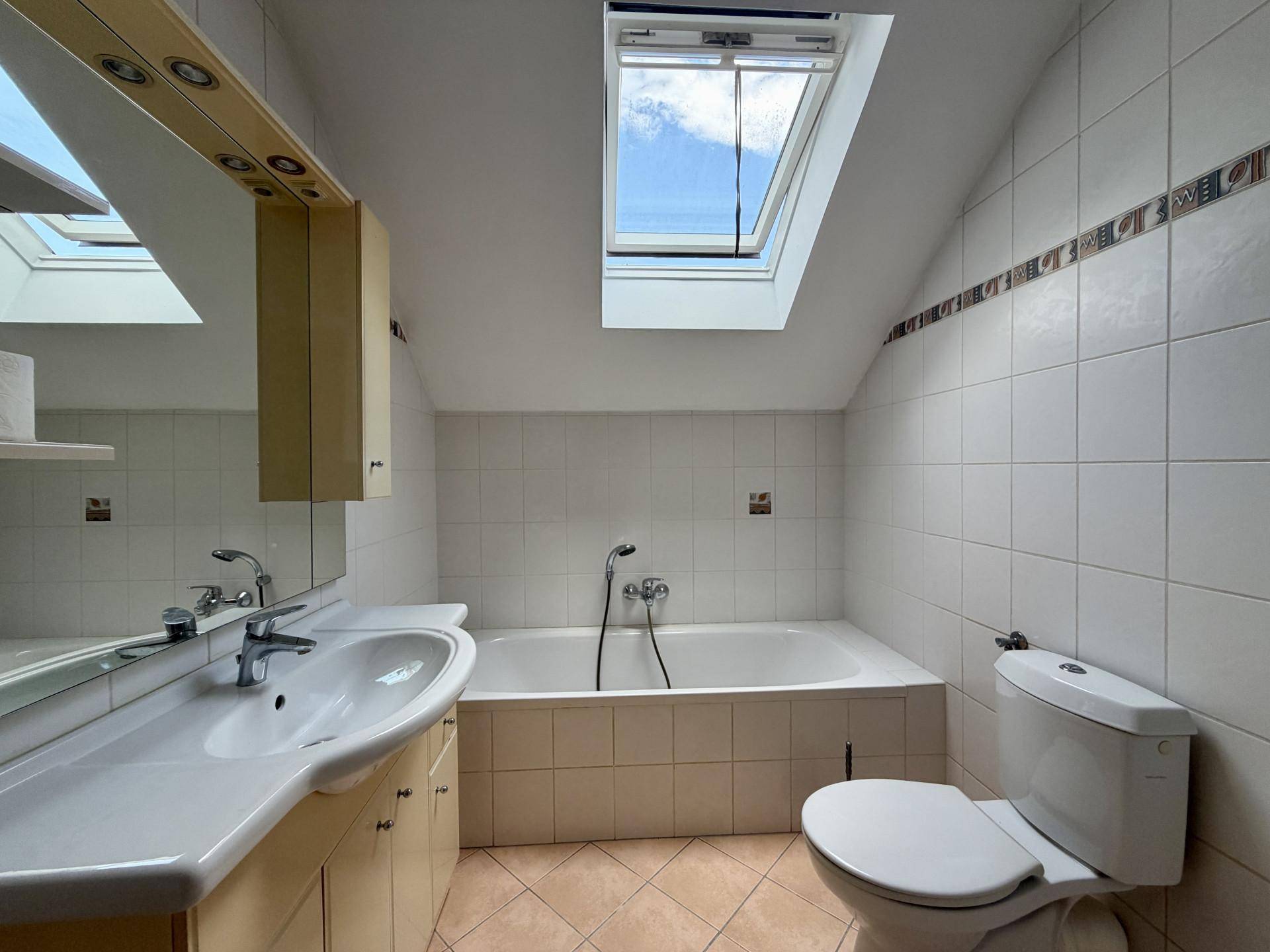 Badezimmer mit Badewanne, Waschbecken, Toilette und Dachfenster, hell gefliest und funktional.