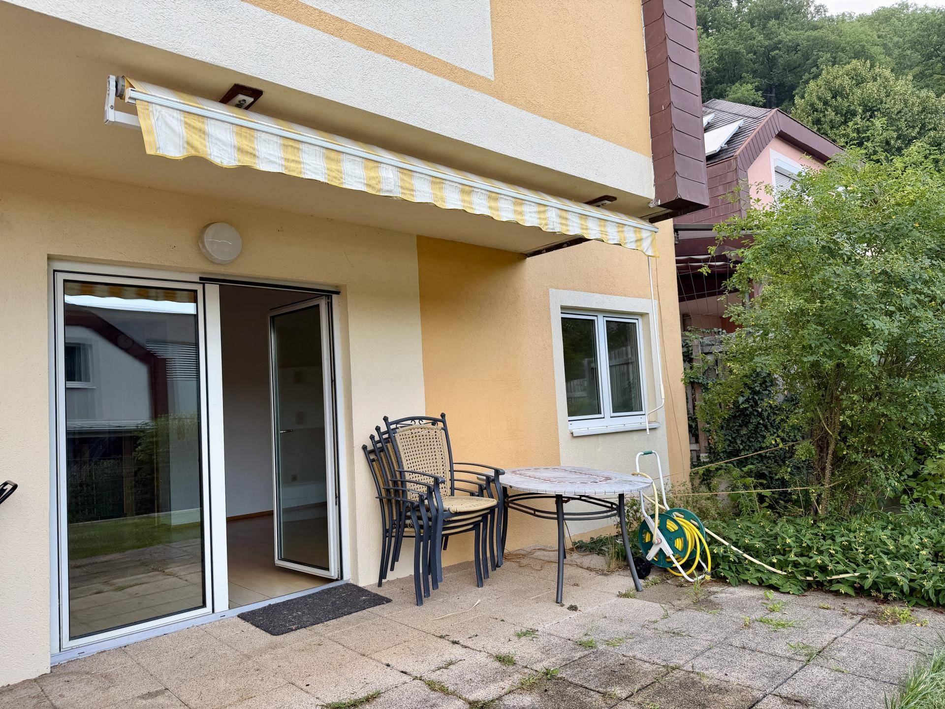 Terrasse mit Gartenmöbeln und ausziehbarer gelb-weiß gestreifter Markise, ideal für entspannte Stunden.