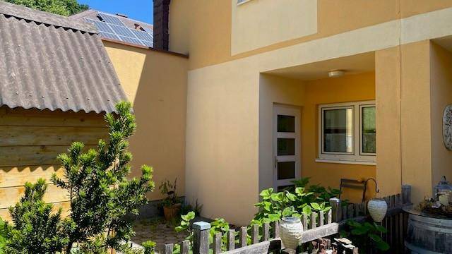 Seitenansicht des Hauses mit kleinem umzäunten Gartenbereich und Eingang, umgeben von Grün.