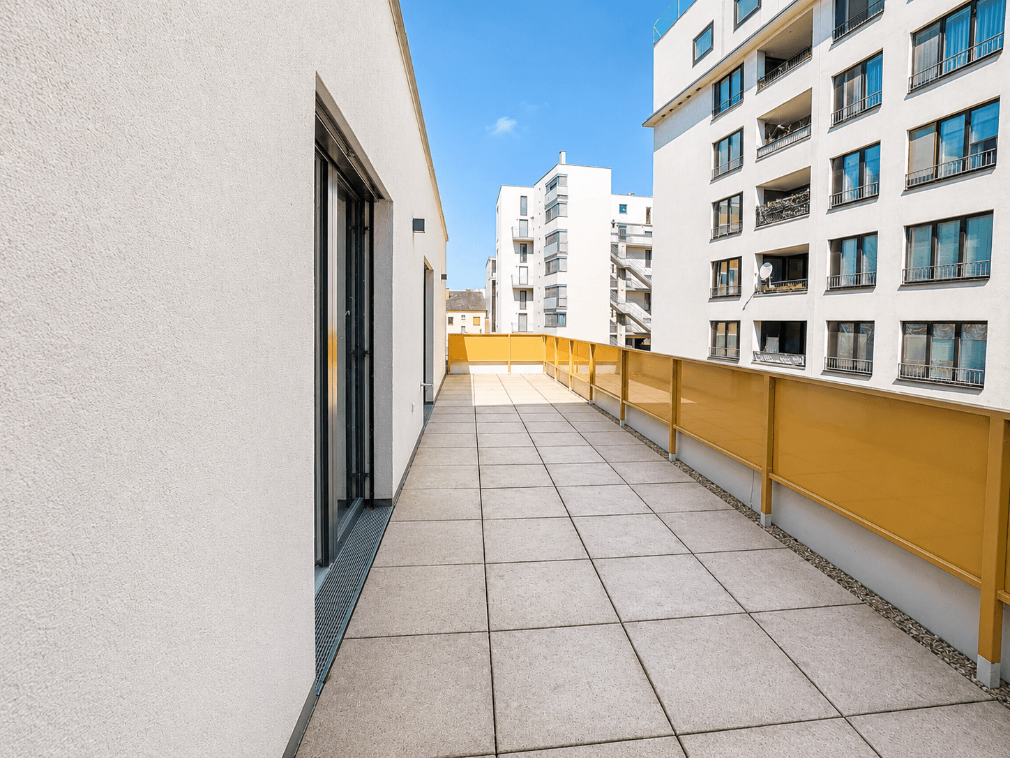 Große, sonnige Terrasse mit modernen Fliesen und Blick auf umliegende Neubauten in urbaner Umgebung.