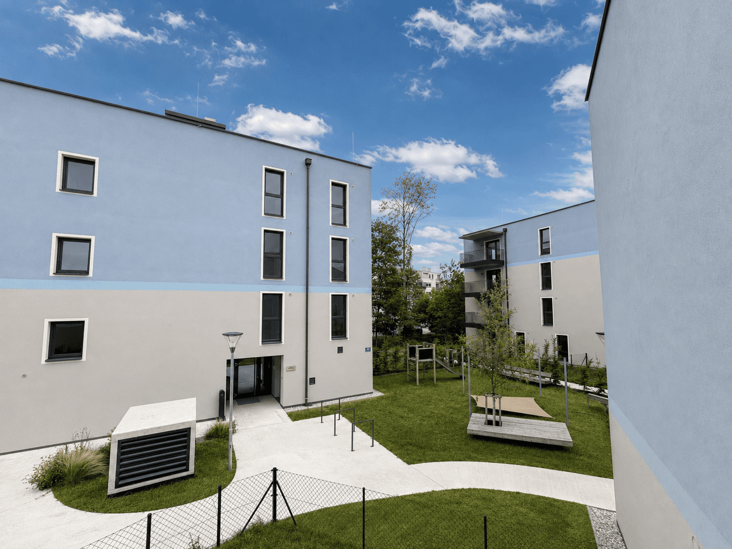 Ansicht der modernen Wohngebäude mit hellblauer Fassade und einem gepflegten Gemeinschaftsgarten.