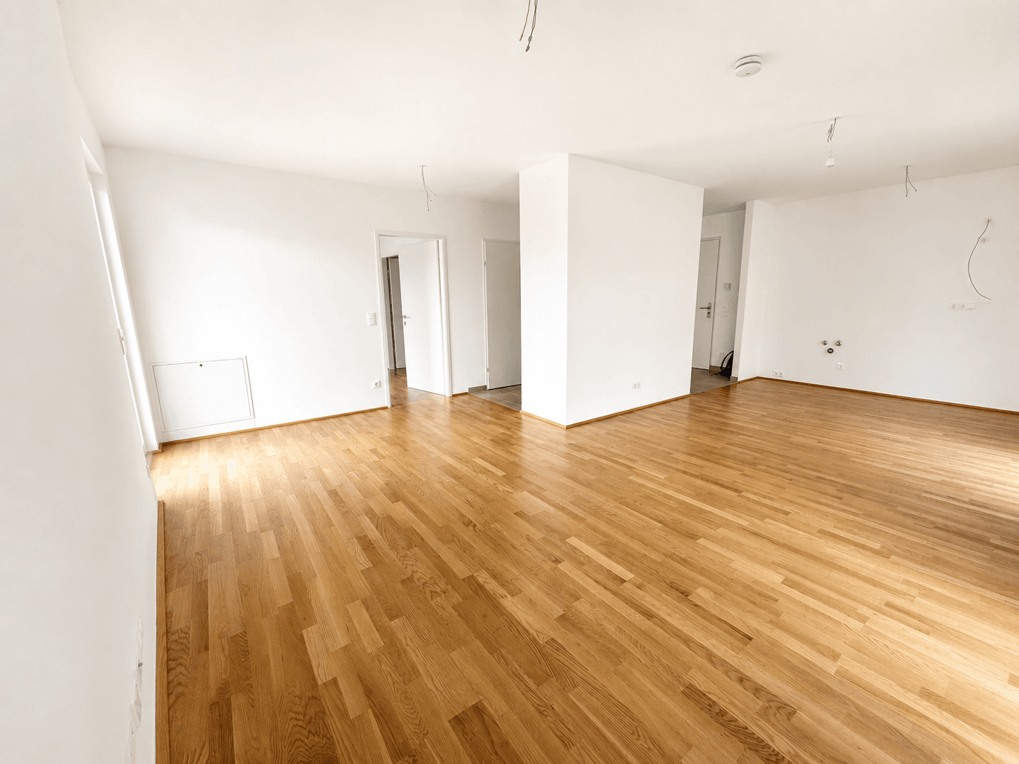 Heller, leerer Wohnbereich mit neuem Holzparkettboden und weißen Wänden, bereit zum Einzug.