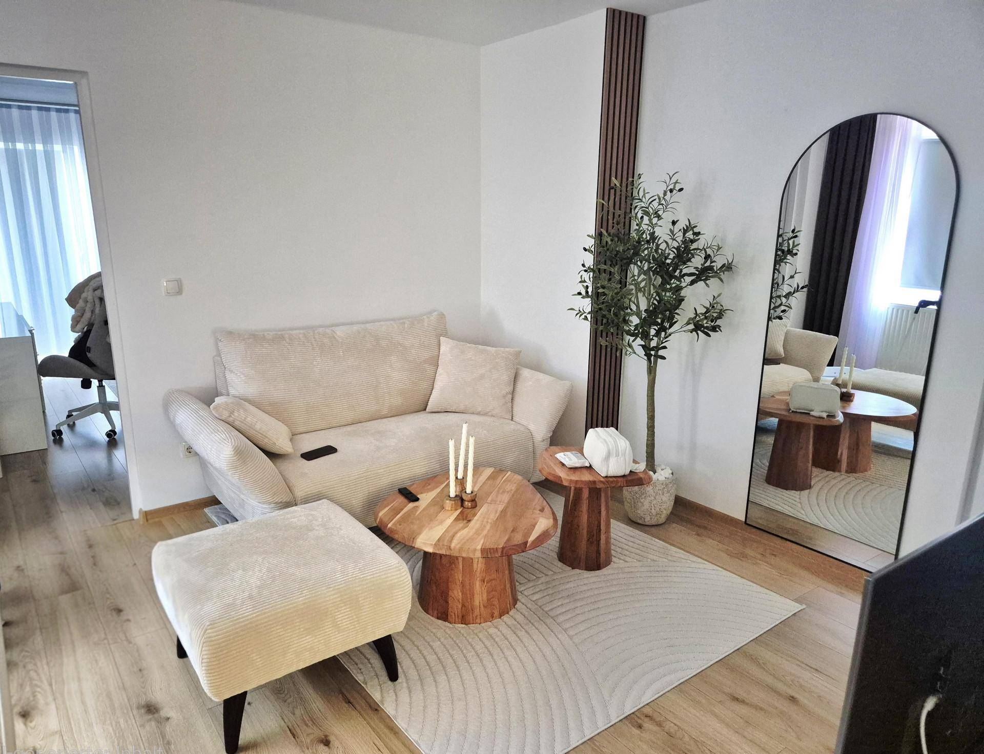 Modernes Wohnzimmer mit beigem Sofa, Holztisch und großem Spiegel, hell und einladend gestaltet.