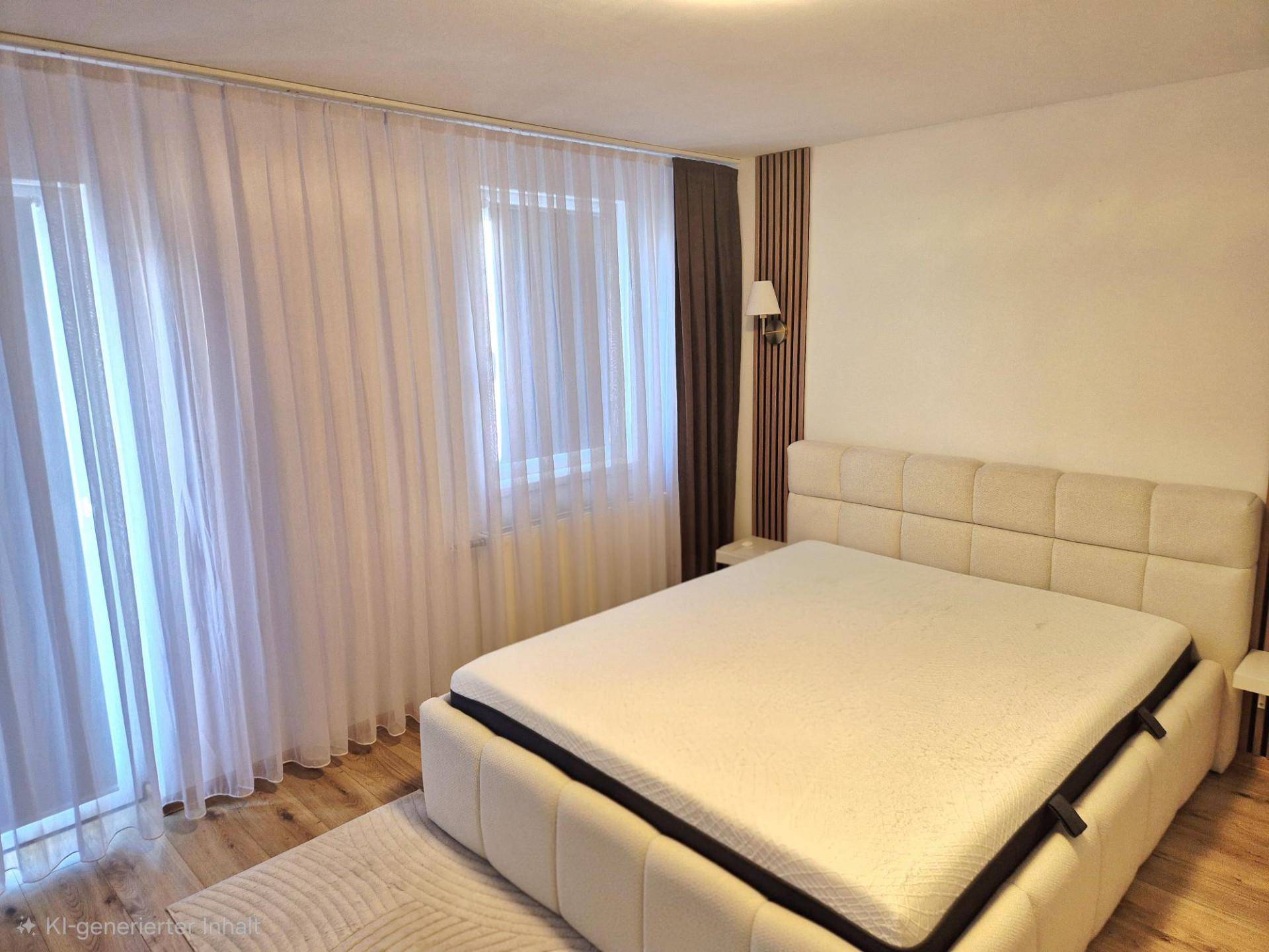 Helles Schlafzimmer mit großem gepolstertem Bett, Holzboden und bodentiefen Fenstern mit Vorhängen.