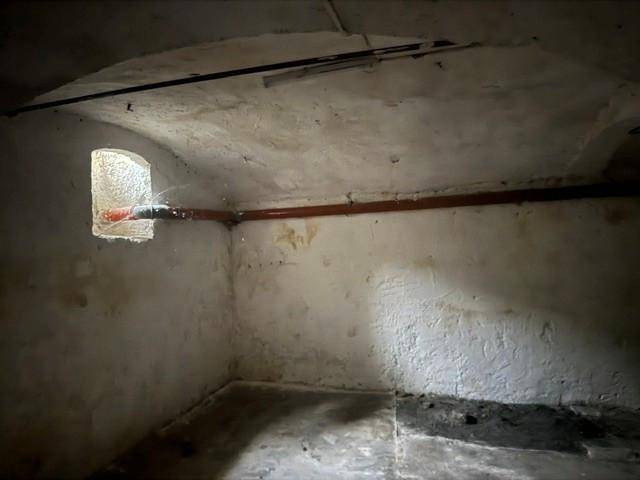 Unausgebauter Kellerraum mit gewölbter Decke, kleinem Fenster und sichtbaren Rohrleitungen.