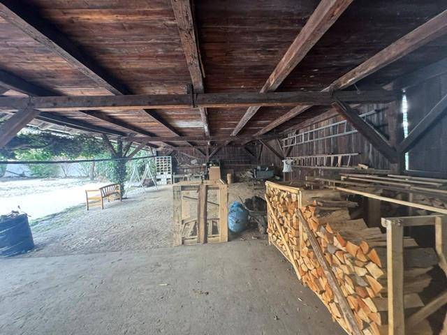 Geräumige Scheune mit Holzdachkonstruktion und gestapeltem Brennholz, ideal für Lagerung.