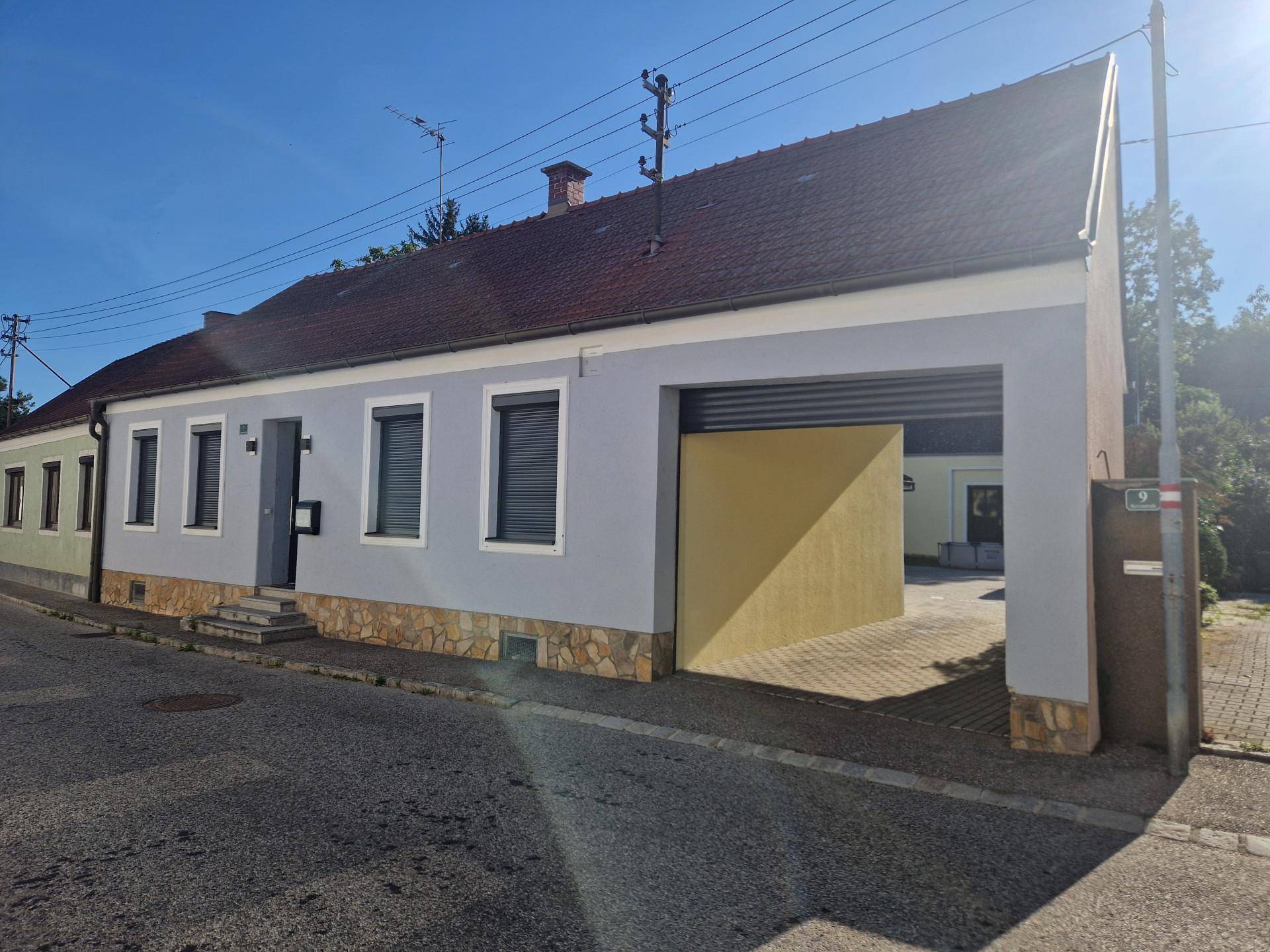 Seitenansicht des Hauses mit grauer Fassade, Rollläden und einem Garagentor an einem sonnigen Tag.