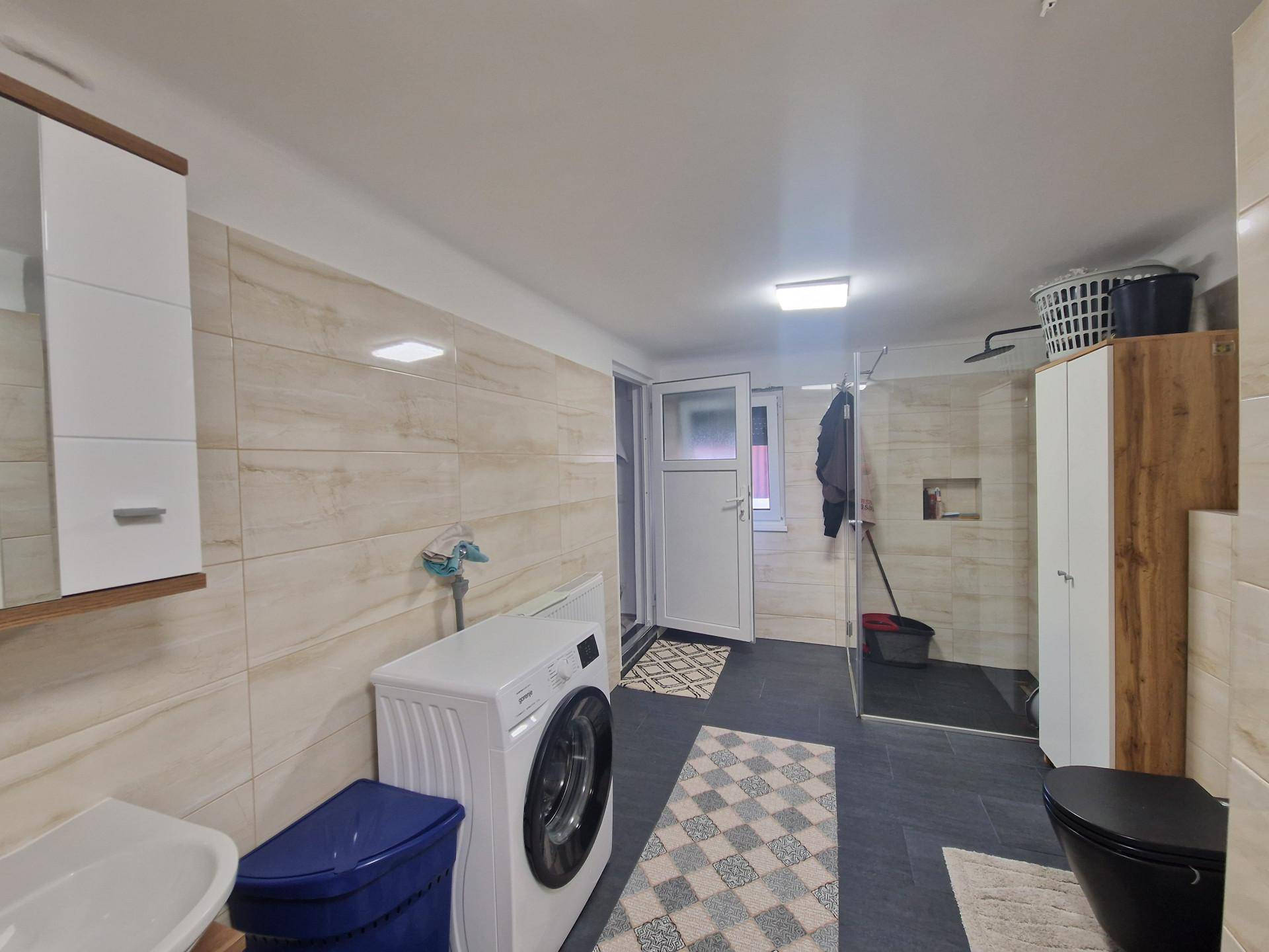 Modernes Badezimmer mit begehbarer Dusche, Waschmaschine und hellen Fliesen.