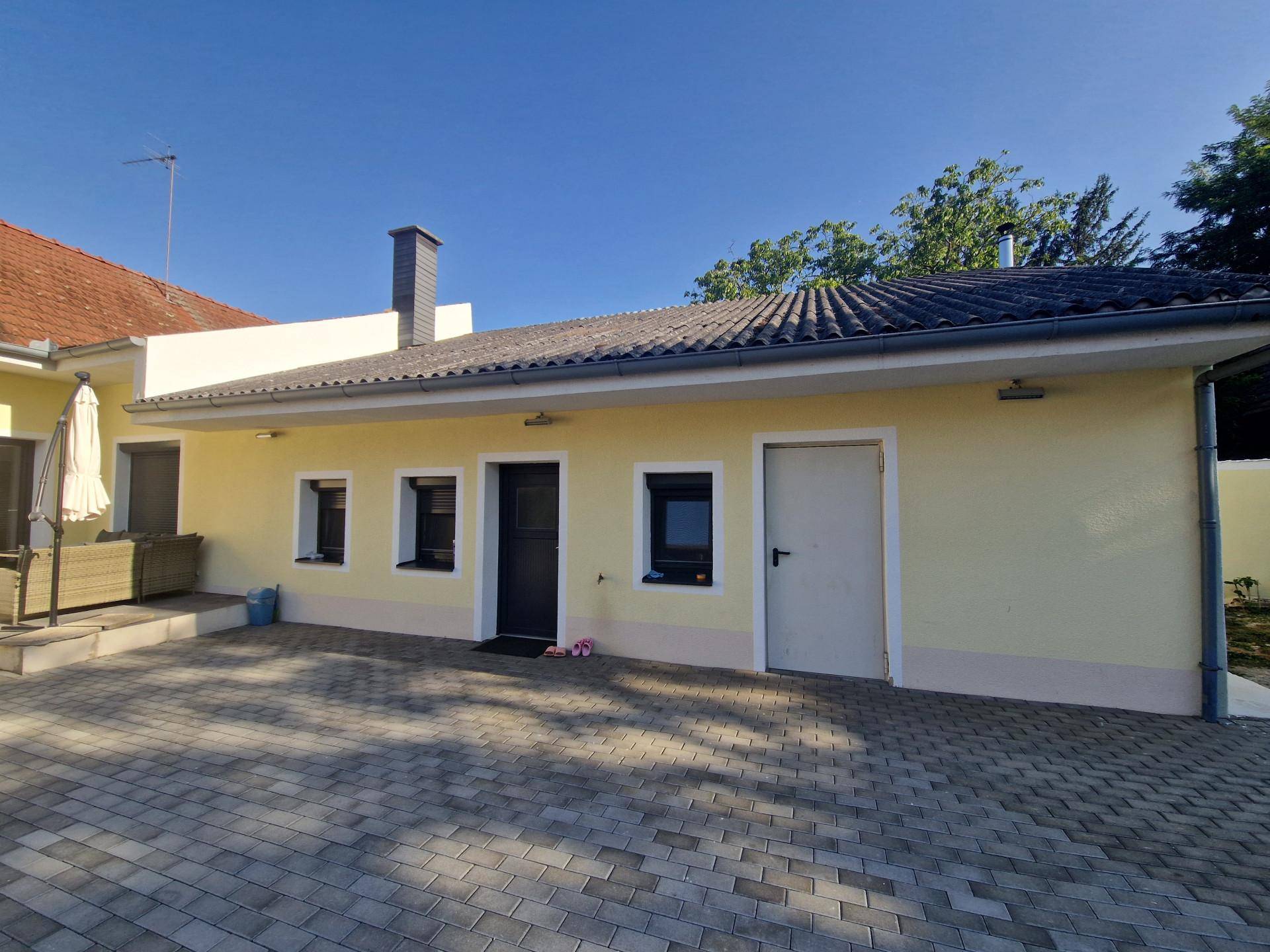 Rückansicht des Hauses mit gepflastertem Hof, gelber Fassade und einem Sonnenschirm.