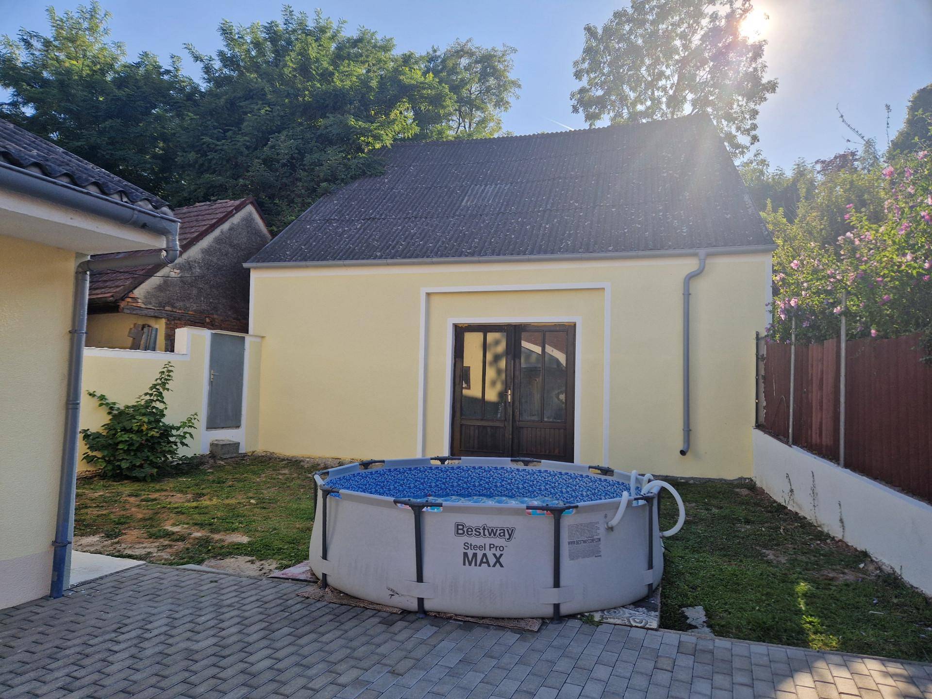Gartenbereich mit einem aufblasbaren Pool, Rasenfläche und einem Nebengebäude im Hintergrund.