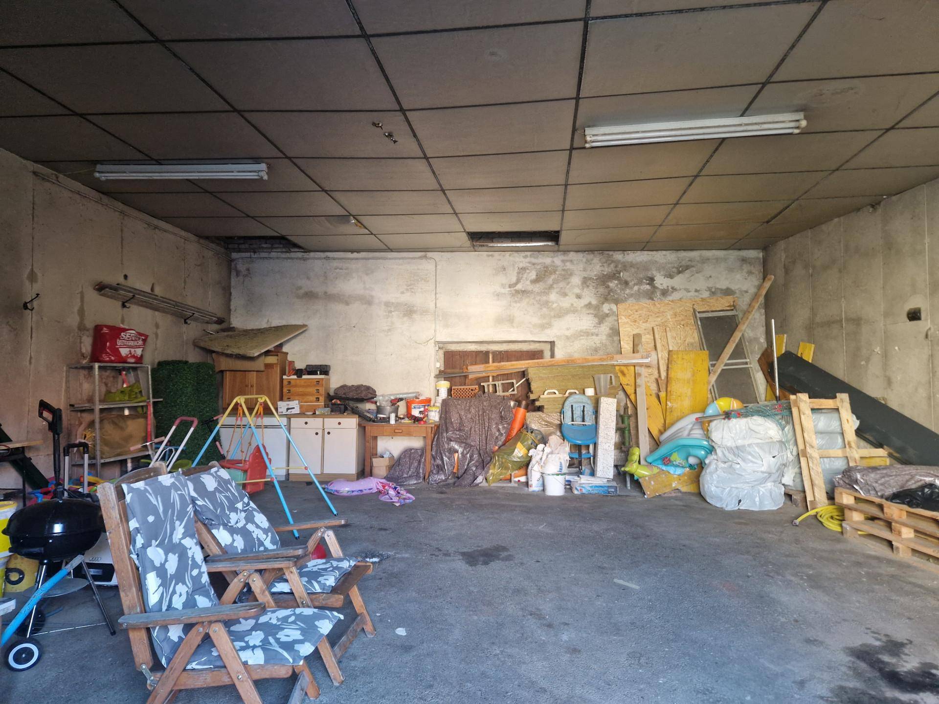 Große Garage oder Lagerraum mit Betonboden und verschiedenen Gegenständen.