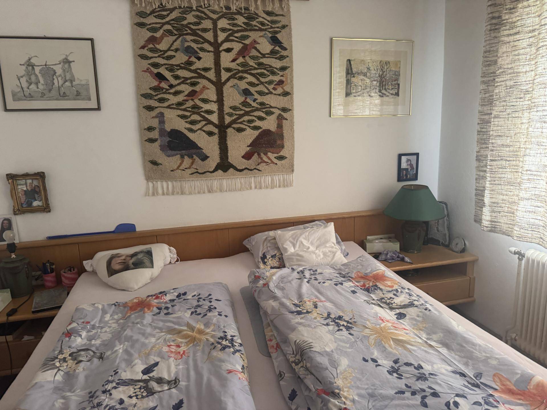 Schlafzimmer mit Doppelbett, Holzmöbeln und einem traditionellen Wandteppich als Dekoration.