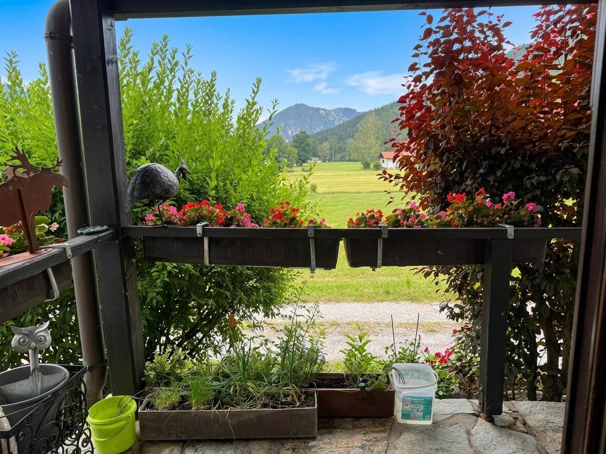 Kleiner Balkon mit Blumenkästen und weitem Blick über die grüne Landschaft und Berge.