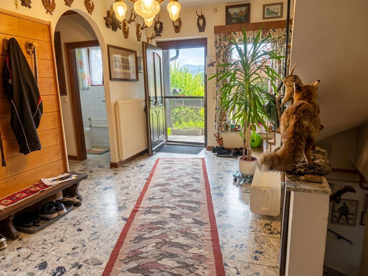 Geräumiger Eingangsbereich mit Terrazzoboden, Garderobe und Blick ins Grüne durch die Haustür.