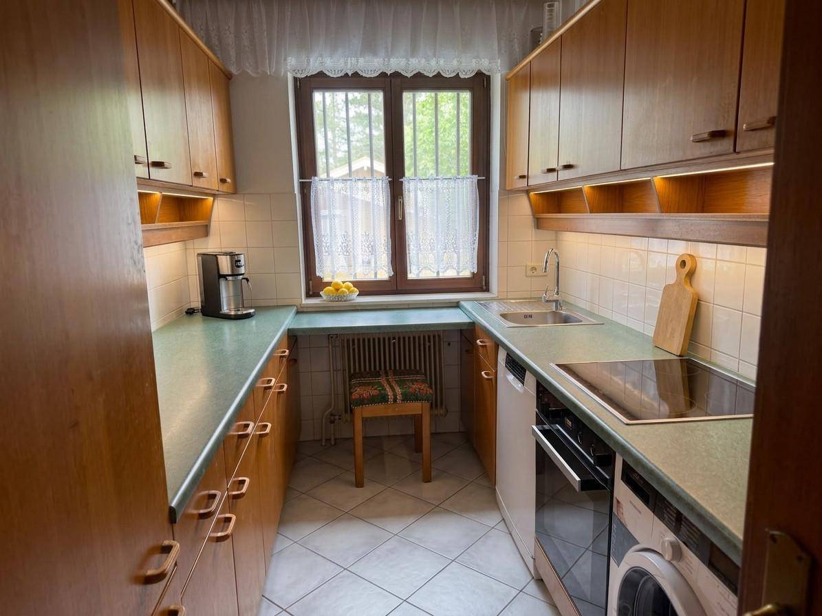 Kleine Küche mit Holzschränken, hellgrüner Arbeitsplatte und einem Fenster mit Vorhängen.