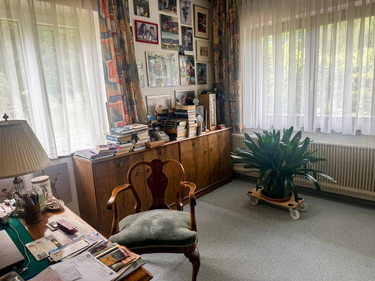 Helles Arbeitszimmer mit großem Schreibtisch, Holzschrank und vielen Fenstern für Tageslicht.