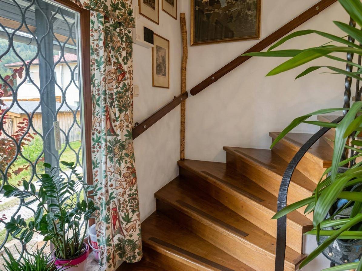 Holztreppe mit schmiedeeisernem Geländer und einem großen Fenster mit dekorativem Gitter.