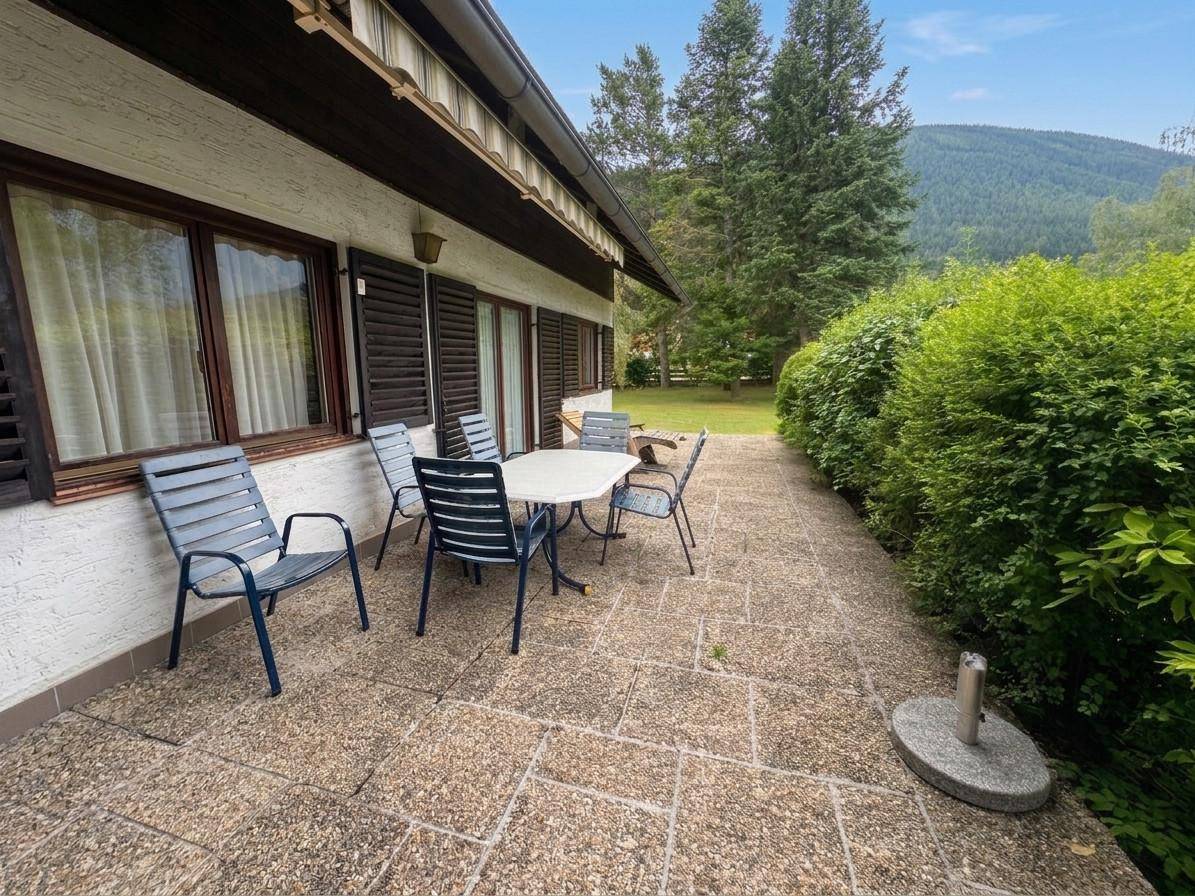 Lange Terrasse entlang des Hauses mit Sitzgelegenheiten und einer dichten grünen Hecke.