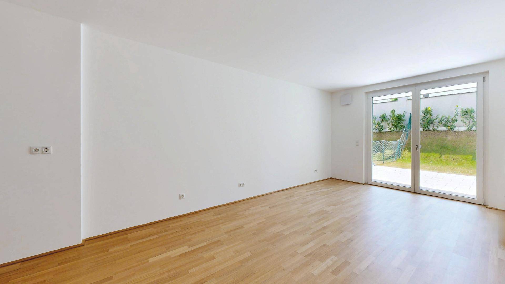 Heller, leerer Raum mit Holzboden und großen Fenstern zum Garten, ideal für Wohnbereich.