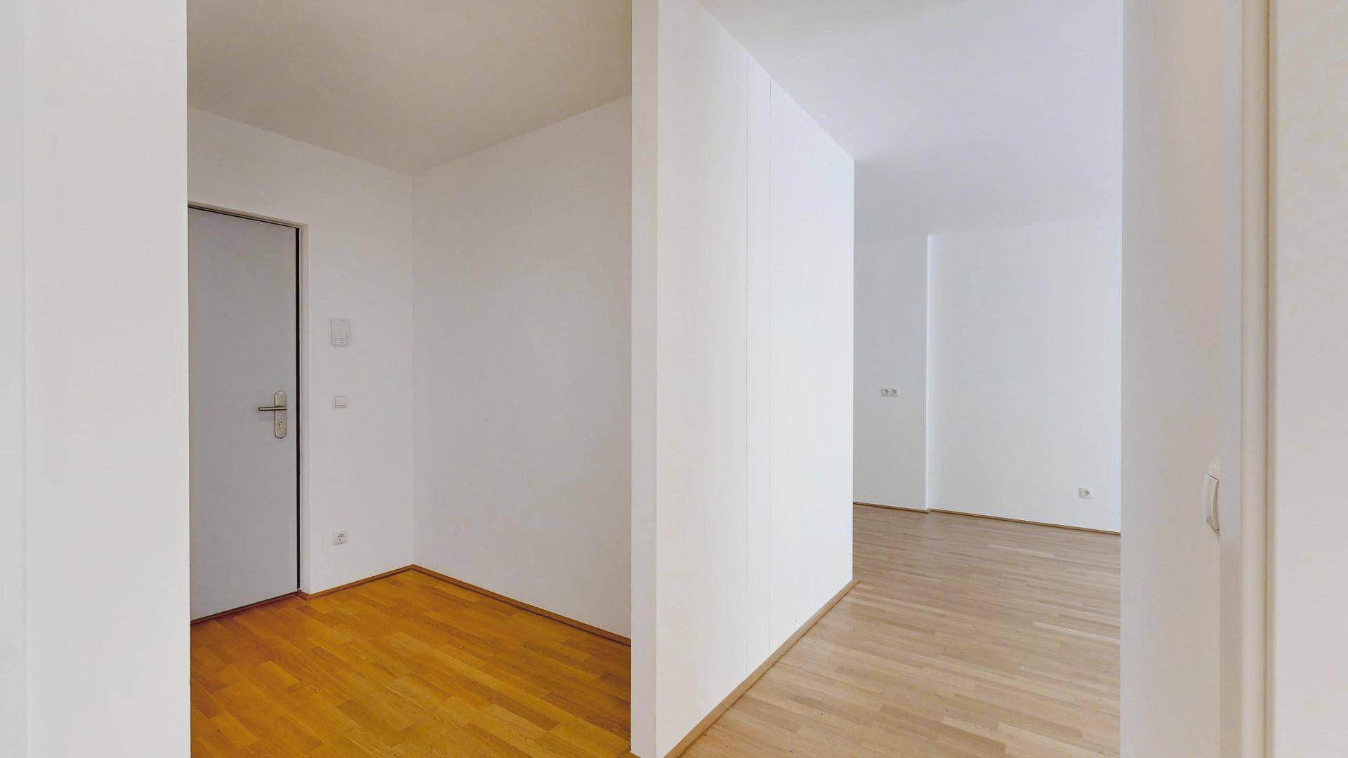 Heller Flur mit Holzboden und weiß gestrichenen Wänden, verbindet verschiedene Räume.