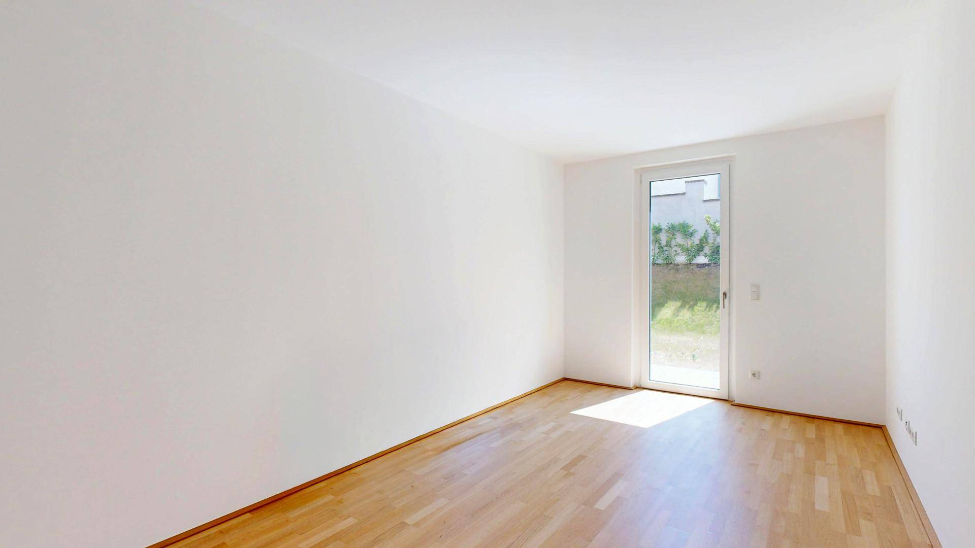 Helles Schlafzimmer mit Holzboden und Zugang zum Garten, bereit zur individuellen Gestaltung.