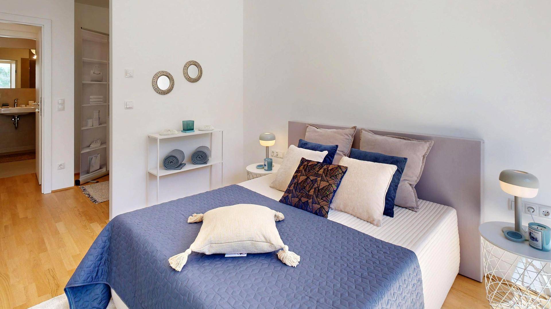 Helles Schlafzimmer mit Doppelbett, Holzboden und direktem Zugang zum Badezimmer.