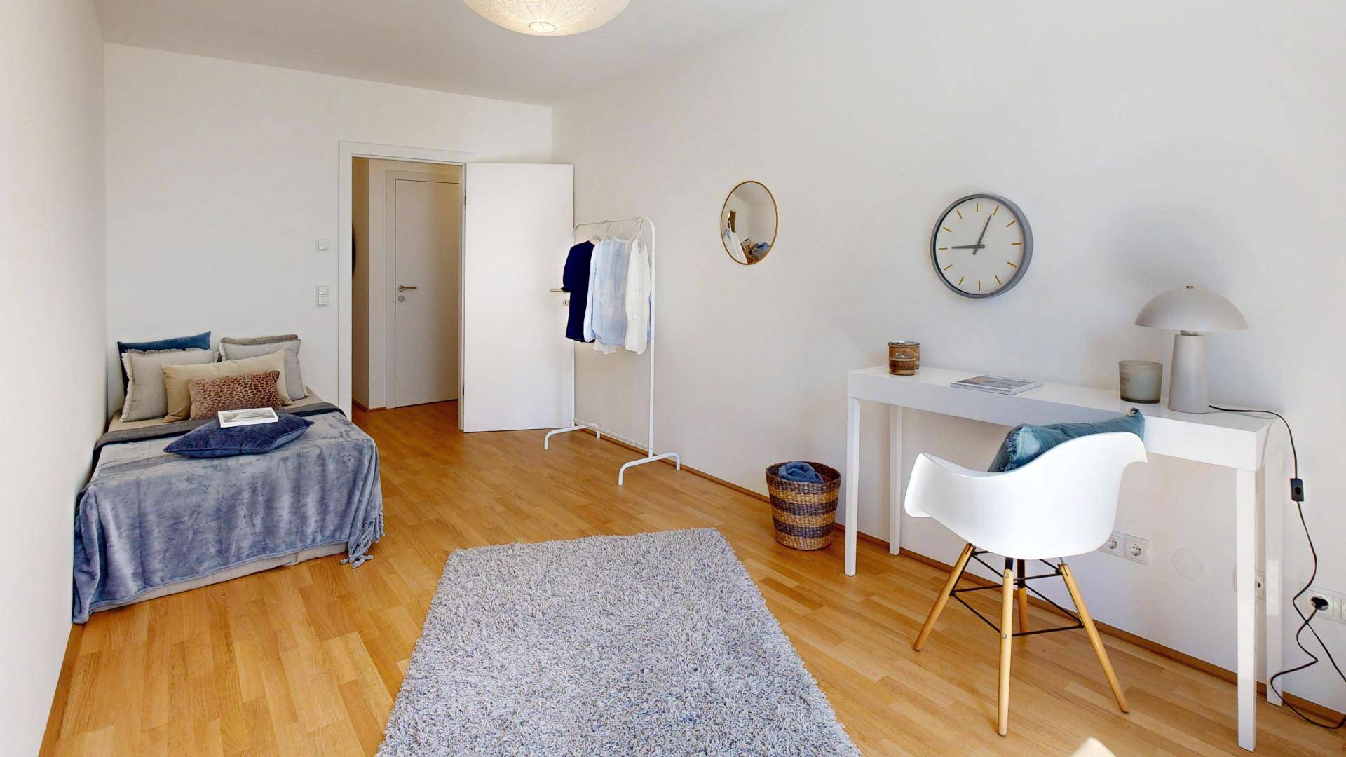 Helles Zimmer, eingerichtet als Schlaf- oder Arbeitszimmer mit Holzboden.
