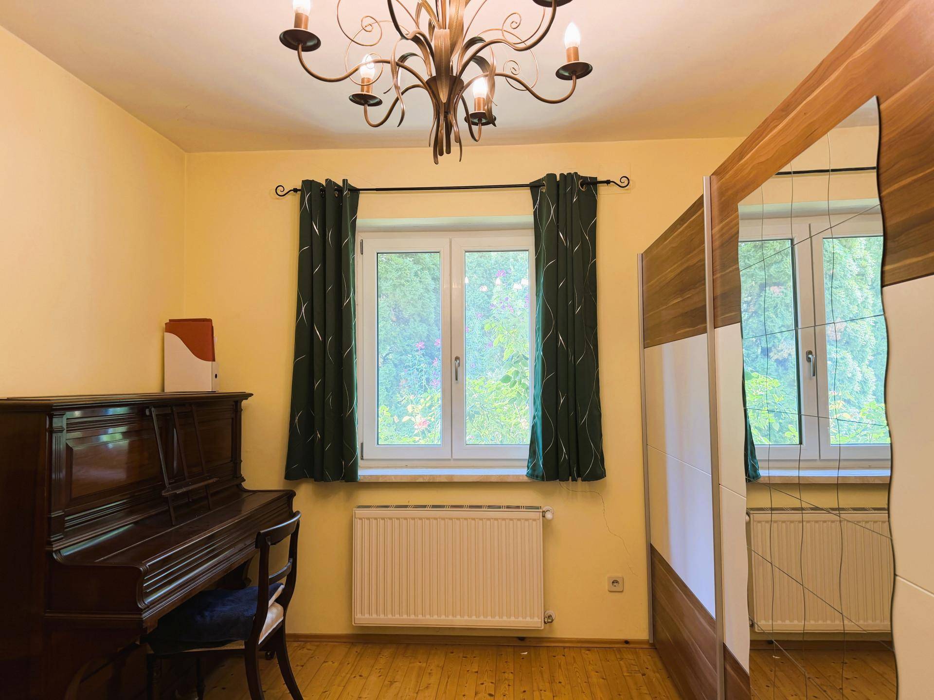 Gemütliches Zimmer mit Holzboden, großem Fenster und einem Kleiderschrank mit Spiegeltüren.