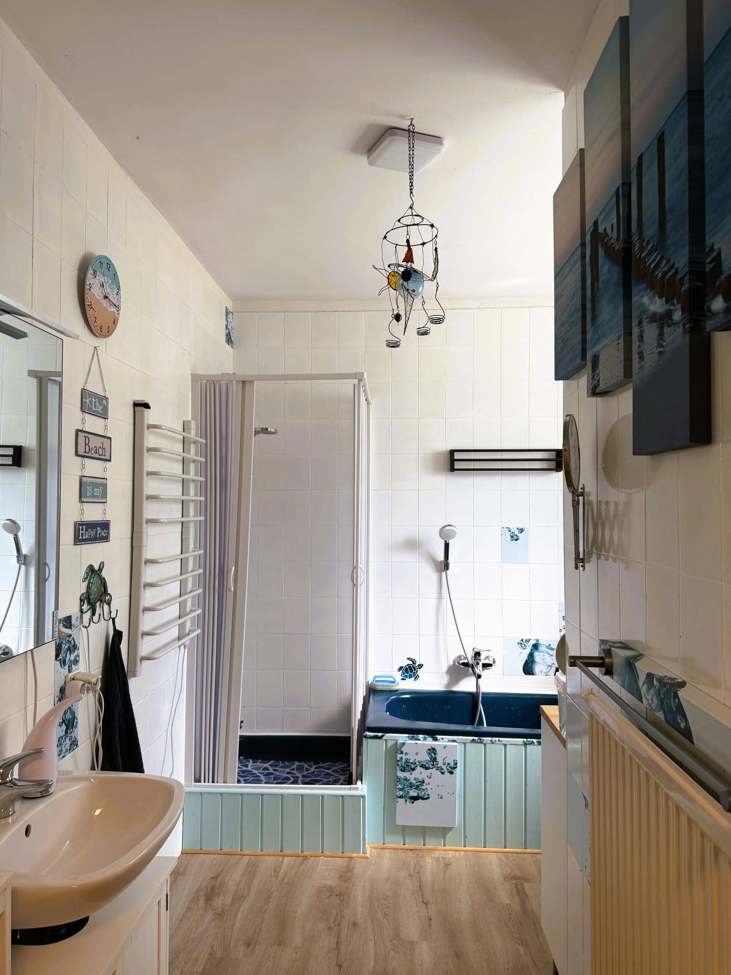 Helles Badezimmer mit Waschtisch, Duschkabine und blauer Badewanne, ausgestattet mit Handtuchheizkörper.