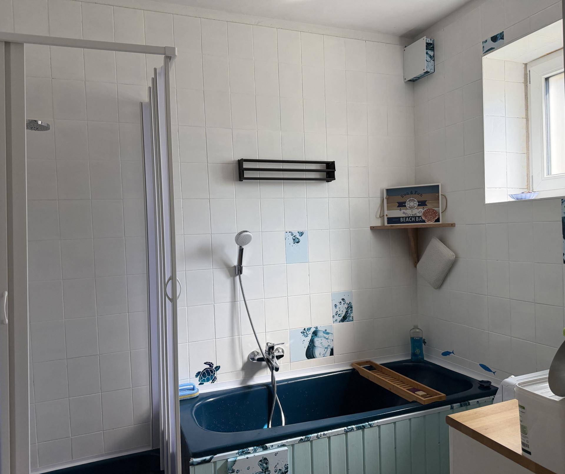 Badezimmer mit blauer Badewanne, Duschkabine und weißen Fliesen, dekoriert mit maritimen Motiven.