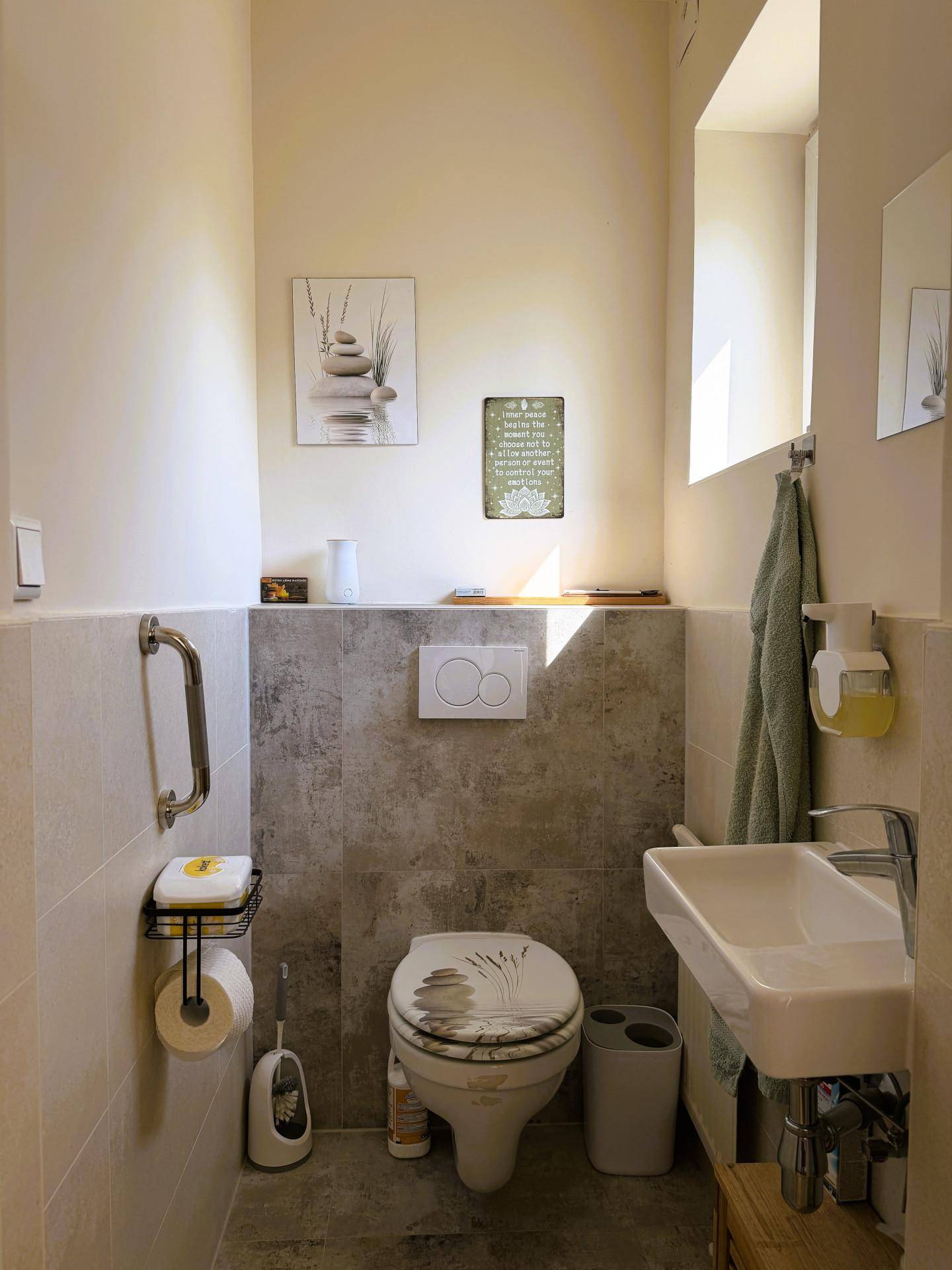 Helles Gäste-WC mit Wand-WC, kleinem Waschbecken und modernen Fliesen in Beige und Grau.