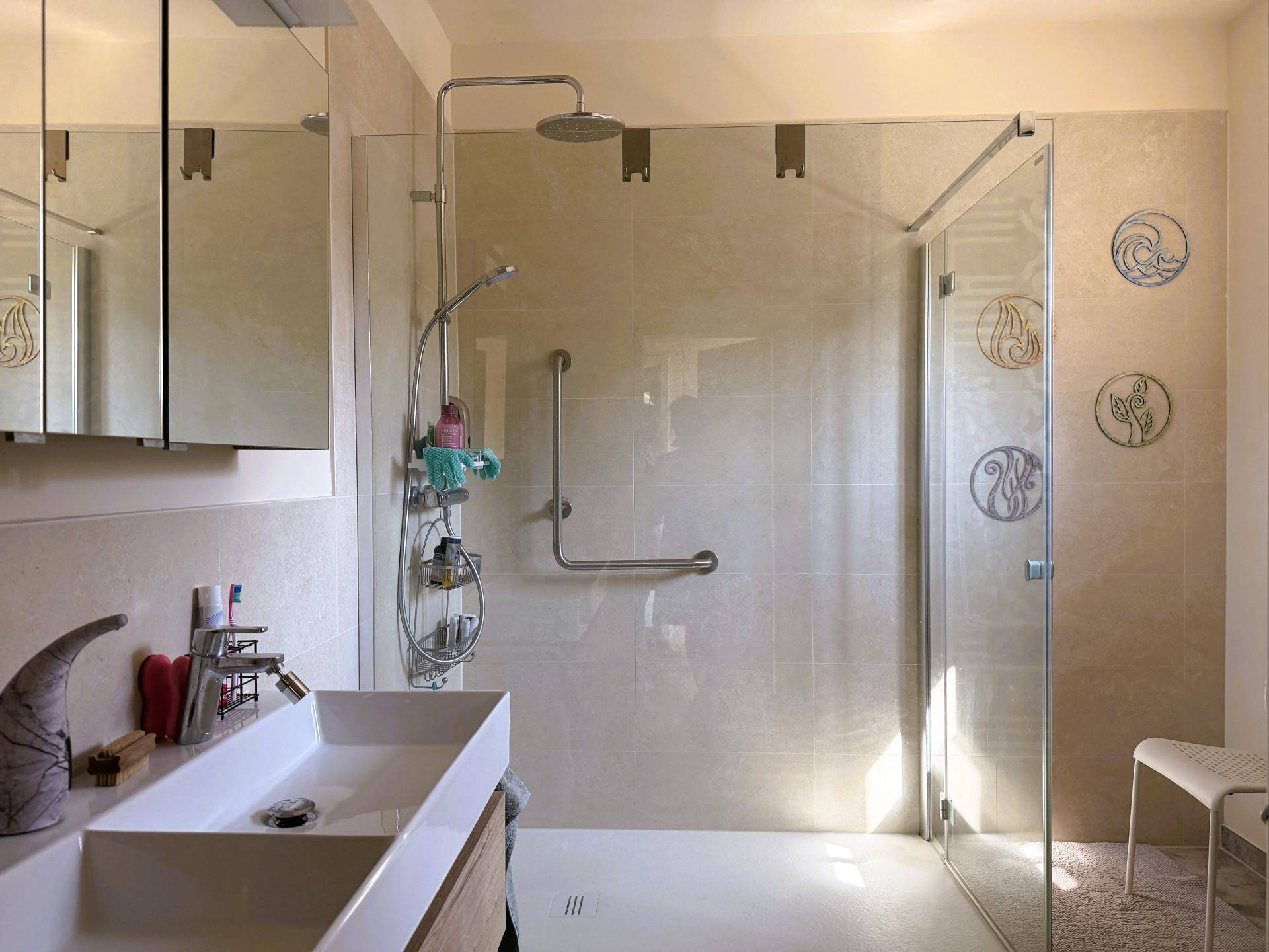 Modernes Badezimmer mit großer begehbarer Dusche, Doppelwaschbecken und hellen Fliesen.