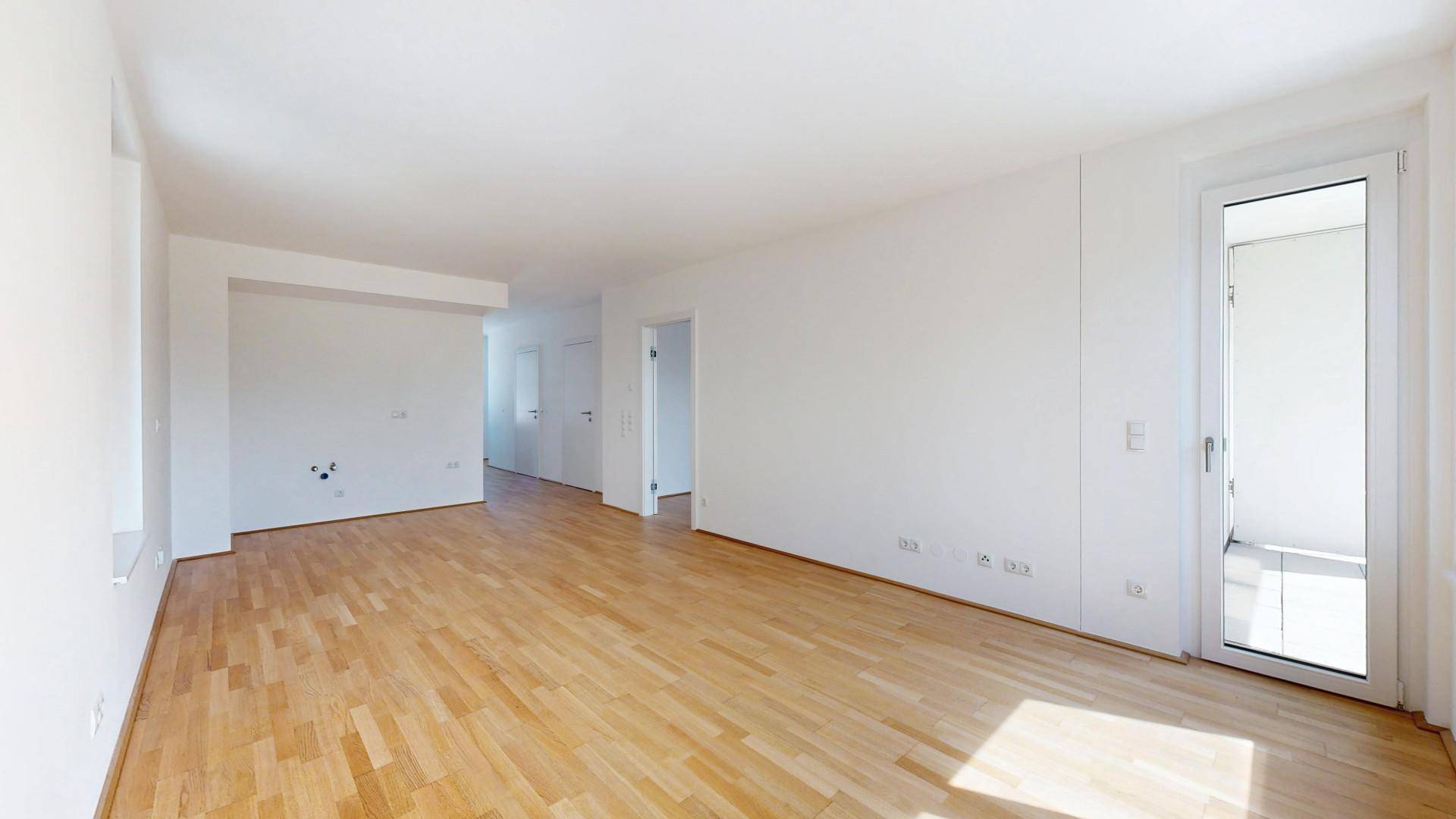Helles, leeres Zimmer mit Parkettboden und Zugang zu einem Balkon, ideal als Wohnbereich.