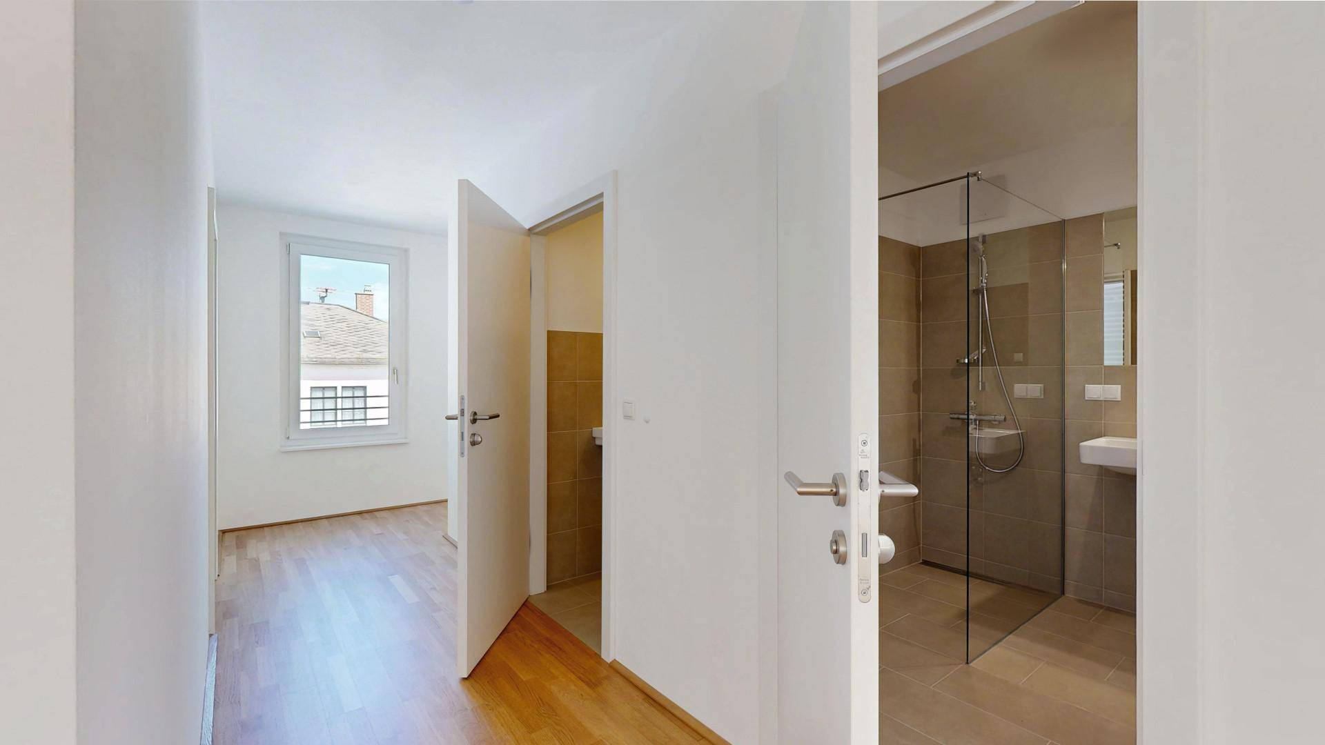Heller Flur mit Parkettboden, der zu einem Zimmer und einem modernen Badezimmer führt.