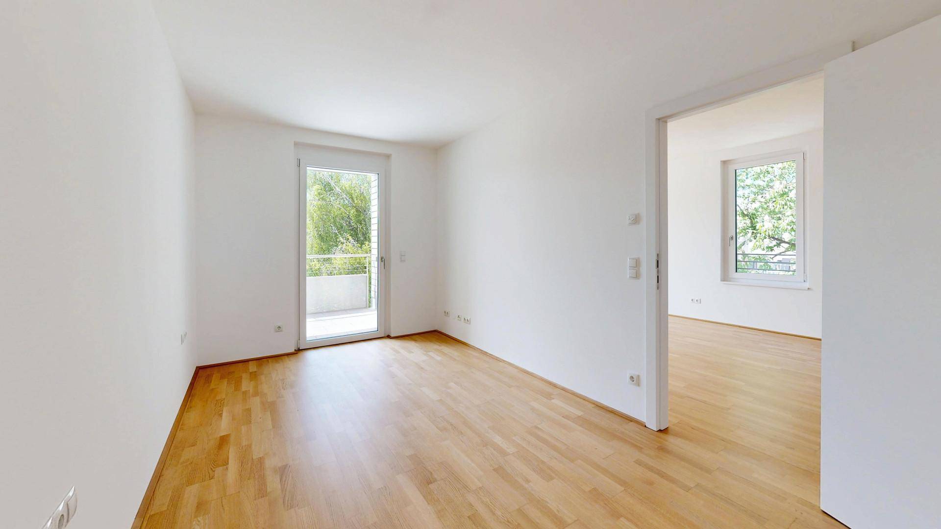 Helles Zimmer mit Parkettboden und direktem Zugang zu einem Balkon, bietet viel Tageslicht.