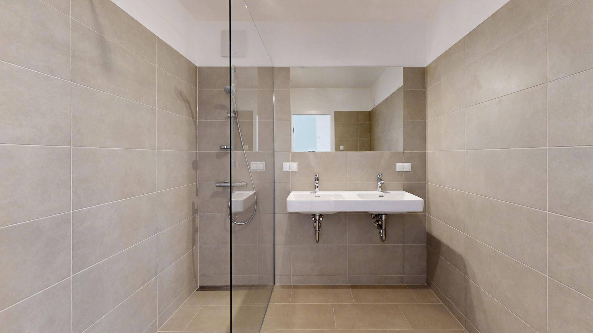 Modernes Badezimmer mit beigefarbenen Fliesen, einer begehbaren Dusche und Doppelwaschbecken.