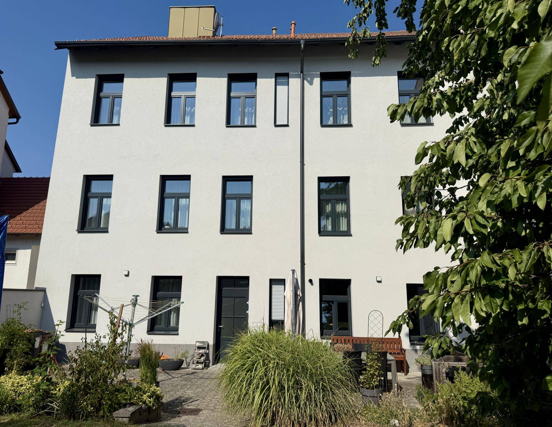 Rückansicht des Gebäudes mit mehreren Fenstern und einem kleinen Gartenbereich, gut gepflegt.