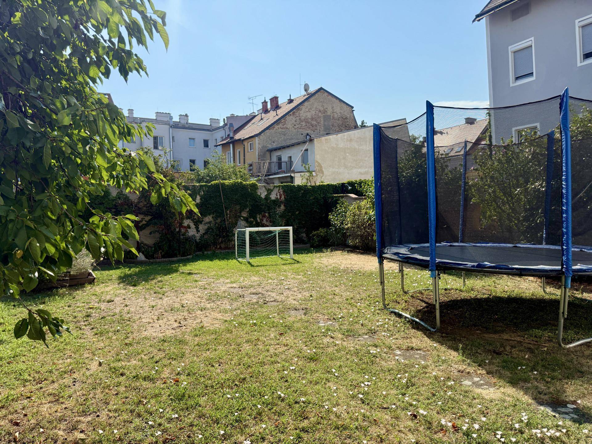 Großer Garten mit Rasenfläche, Trampolin und kleinem Fußballtor für Kinder, sonnig und grün.