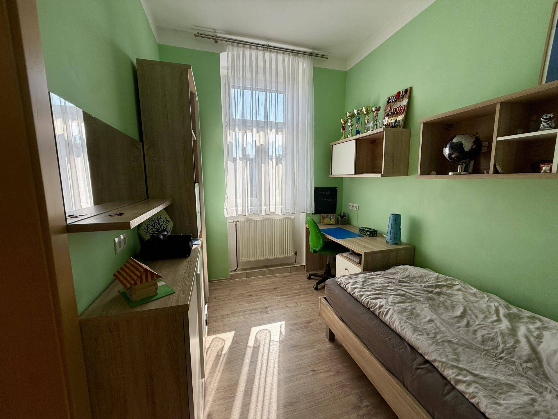 Kinderzimmer mit grün gestrichenen Wänden, Einzelbett und Schreibtisch am Fenster, hell und freundlich.