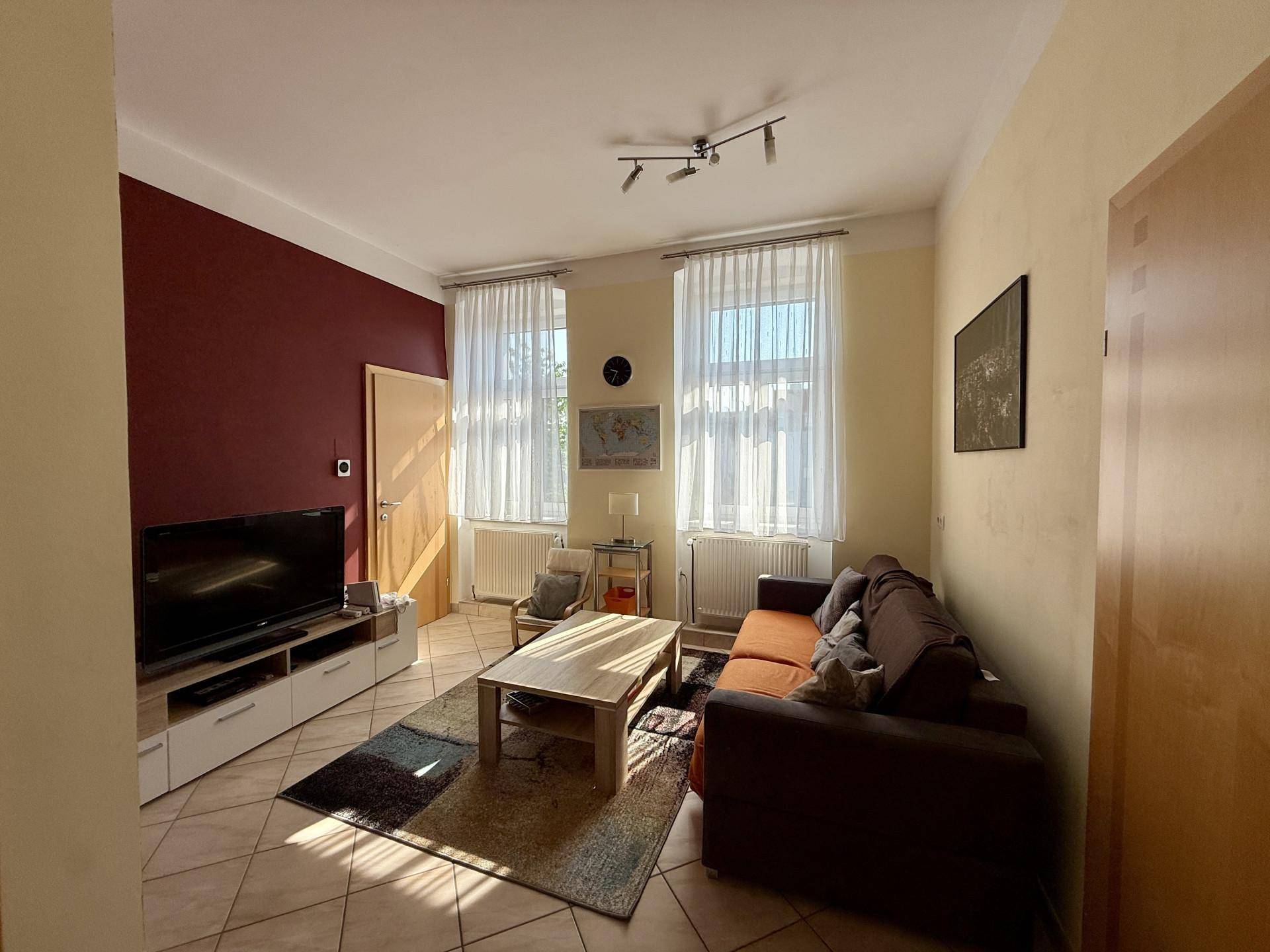 Helles Wohnzimmer mit Fernseher, Sofa und Fliesenboden, durchflutet von Sonnenlicht.