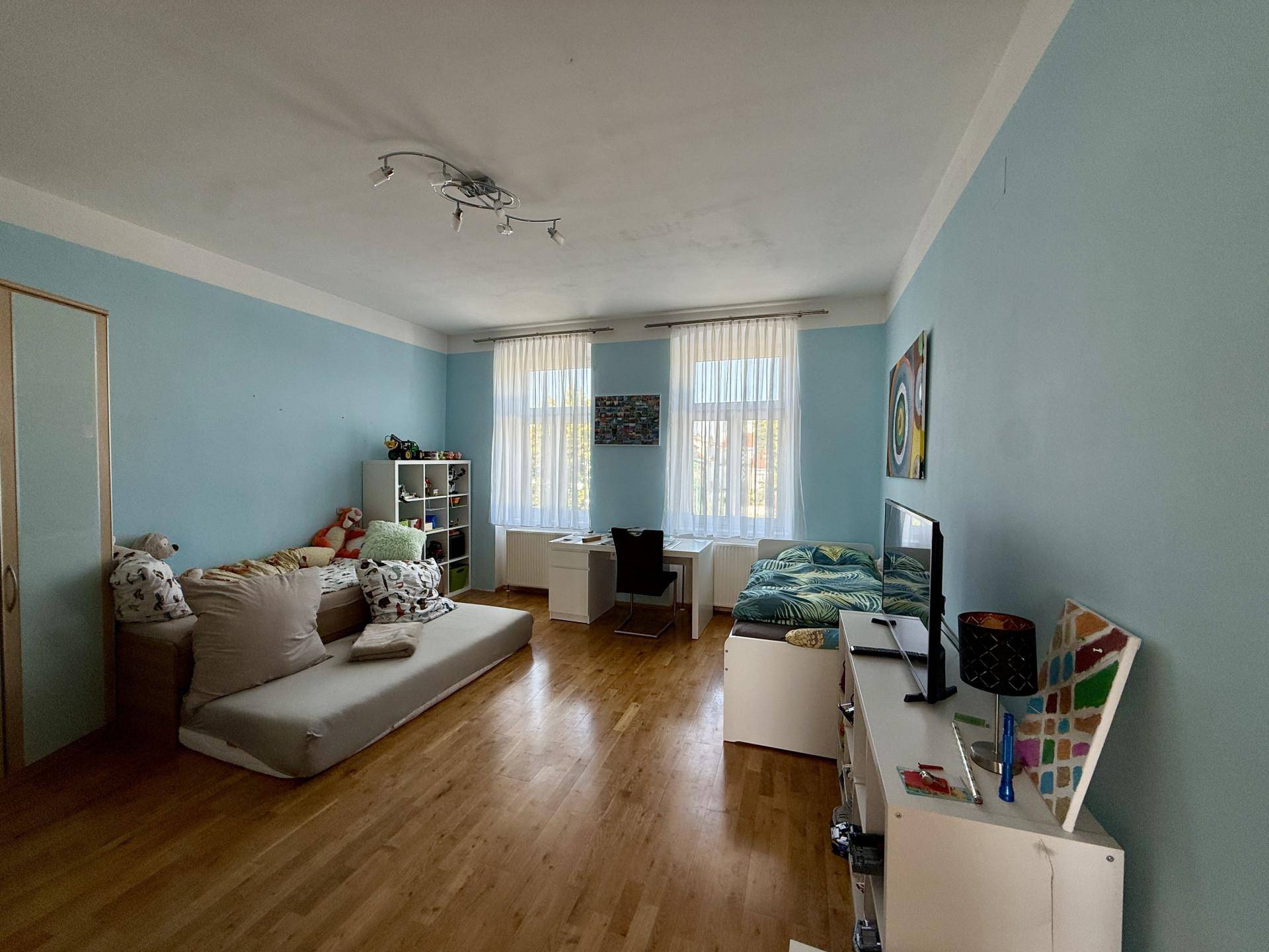 Geräumiges Kinderzimmer mit blauen Wänden, zwei Betten und Holzboden, lichtdurchflutet.