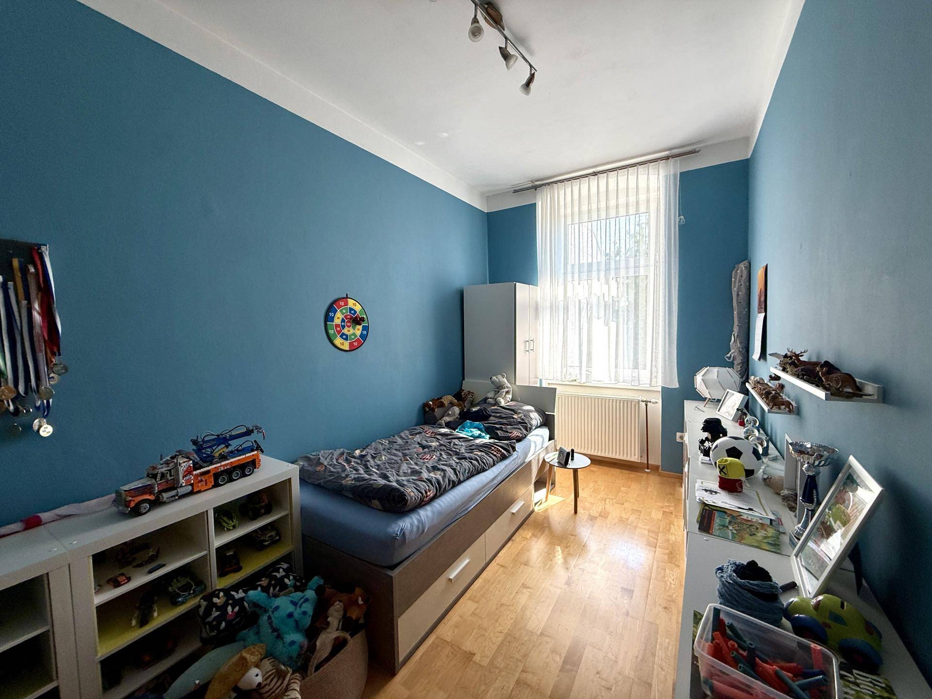 Kinderzimmer mit blauen Wänden, Einzelbett und Spielzeugregalen, hell und funktional eingerichtet.