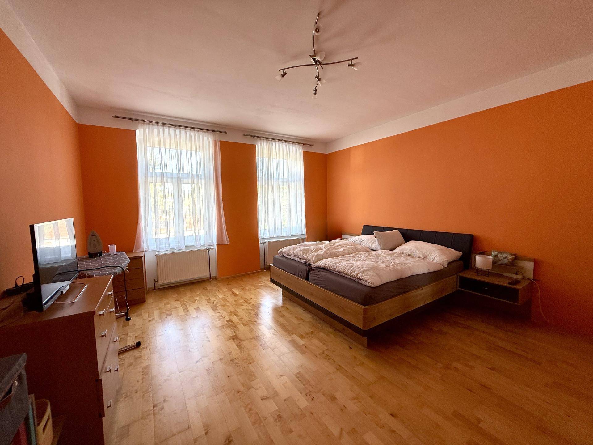 Helles Schlafzimmer mit orangefarbenen Wänden, Doppelbett und Holzboden, sonnig und einladend.