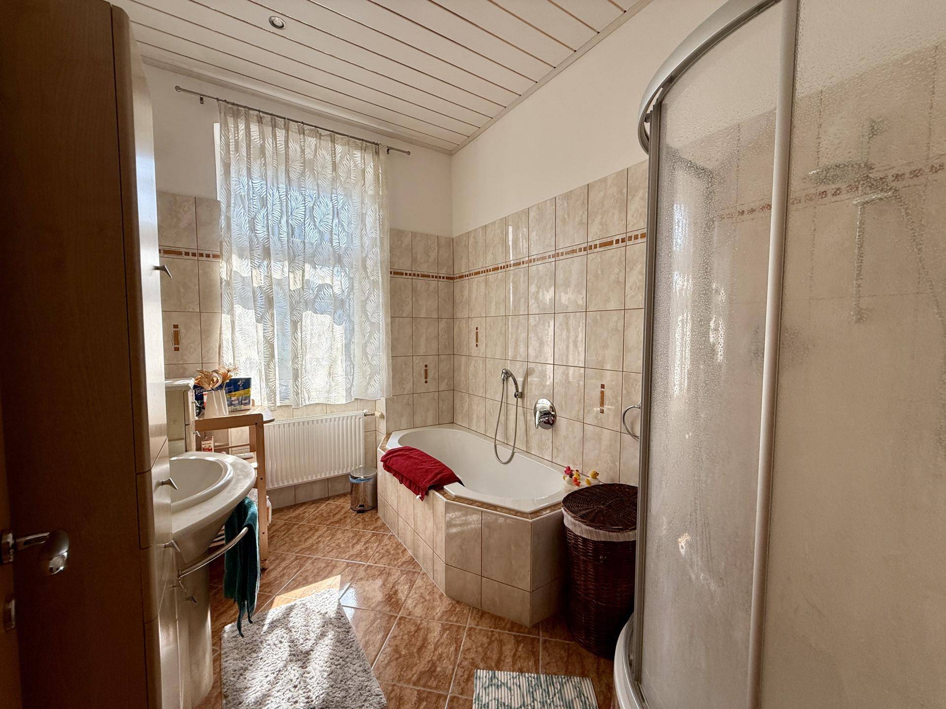 Traditionelles Badezimmer mit Badewanne, Duschkabine und gemusterten Fliesen, gut beleuchtet.